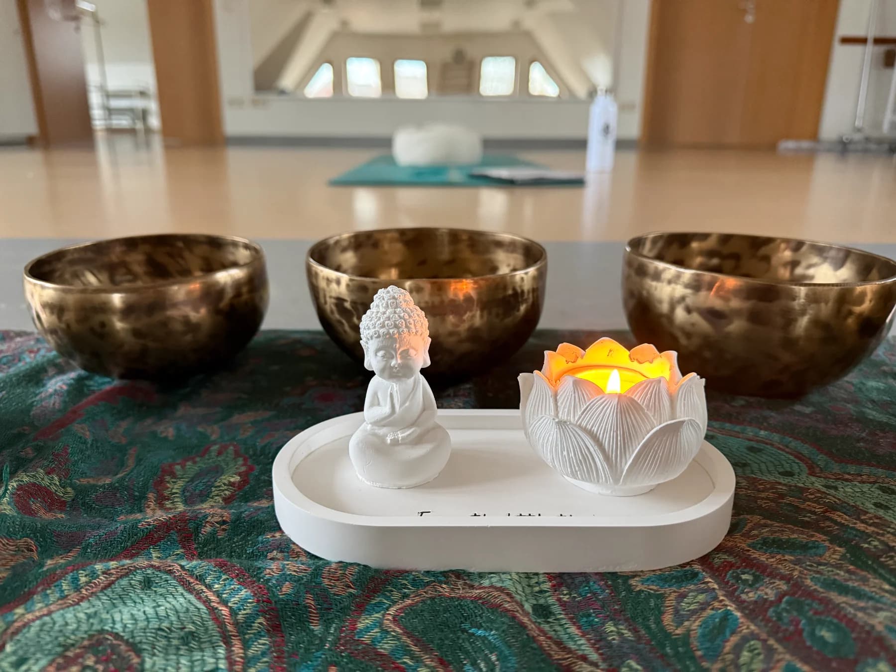 Klangschalen mit Buddha-Figur und Lotuslicht, dahinter der große Saal
